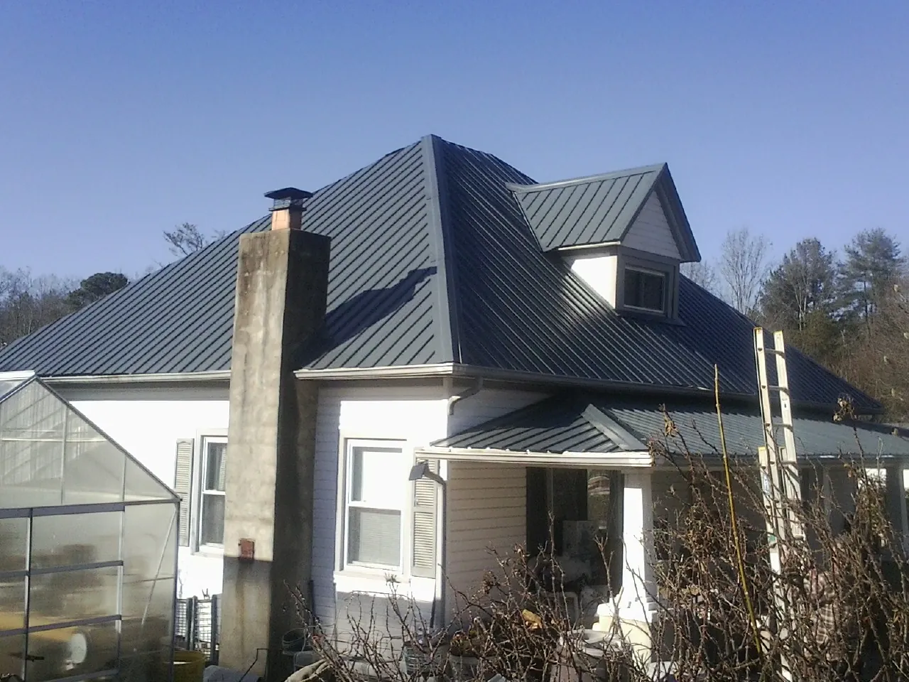 Dark blue standing seam metal roof on a white farmhouse with dormer — Slate & Tile Roof Repair by Roofing Brothers in Morral