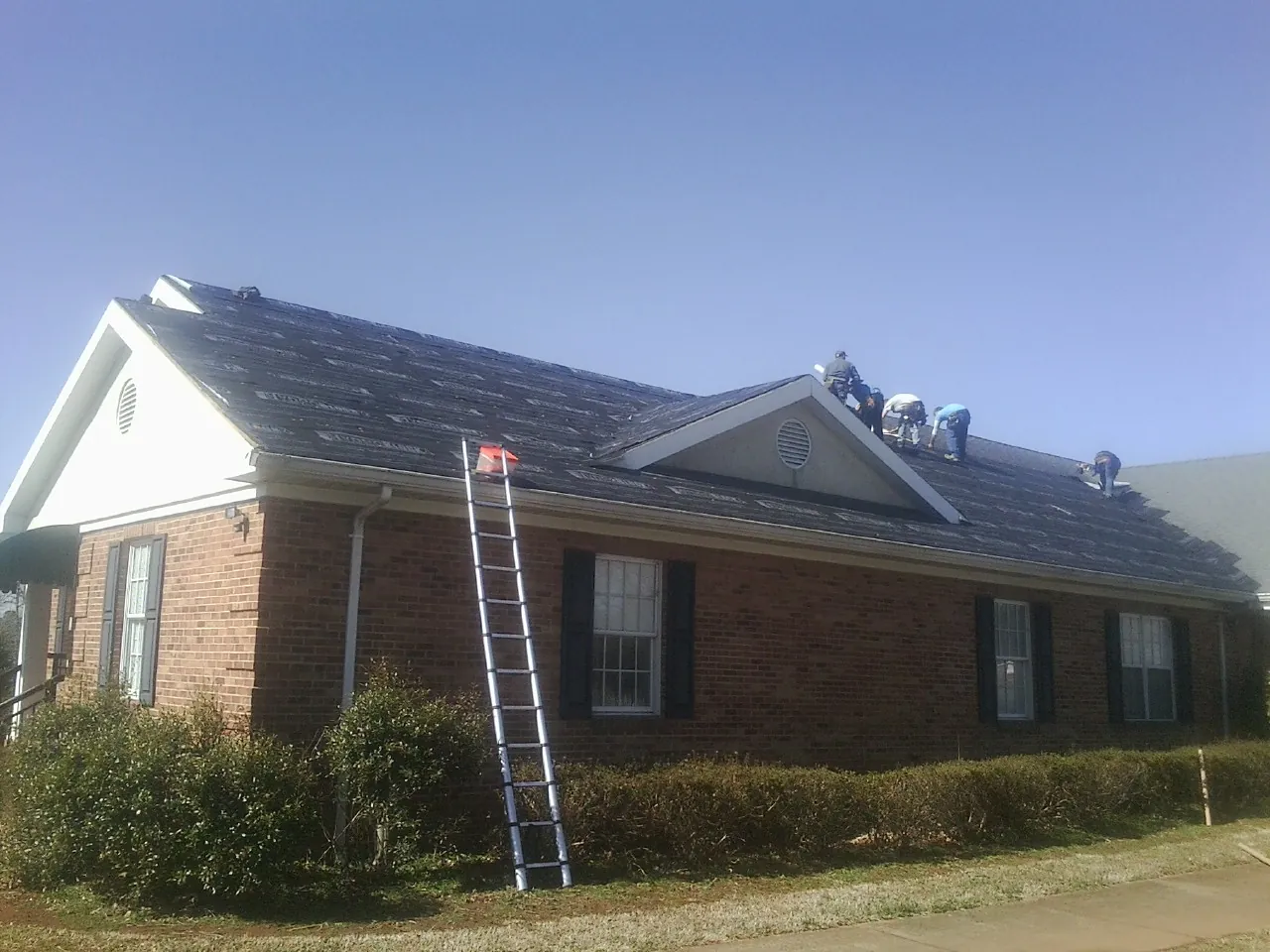Crew tearing shingles off a brick ranch roof with a ladder set — Metal Roof Repair work by our crew in Morral