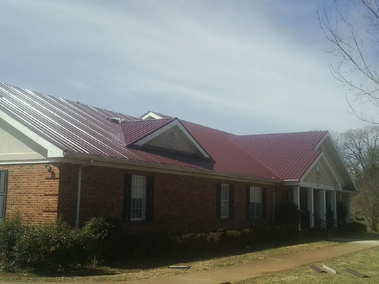 Red metal roof with gabled entries on a long brick building, from a Hail Damage Roof Repair job in Morral