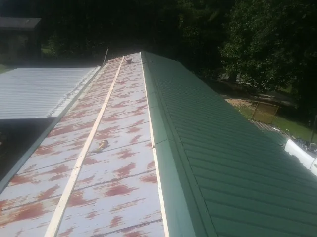 Old rusted panels beside newly installed green metal roofing — Wind Damage Roof Repair by Roofing Brothers in Morral