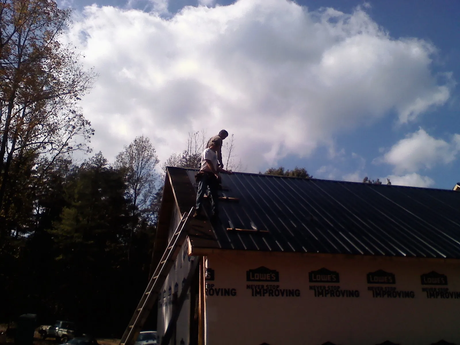 Roofer fastening dark metal panels high against a cloudy sky, from a Roof Inspection job in Morral