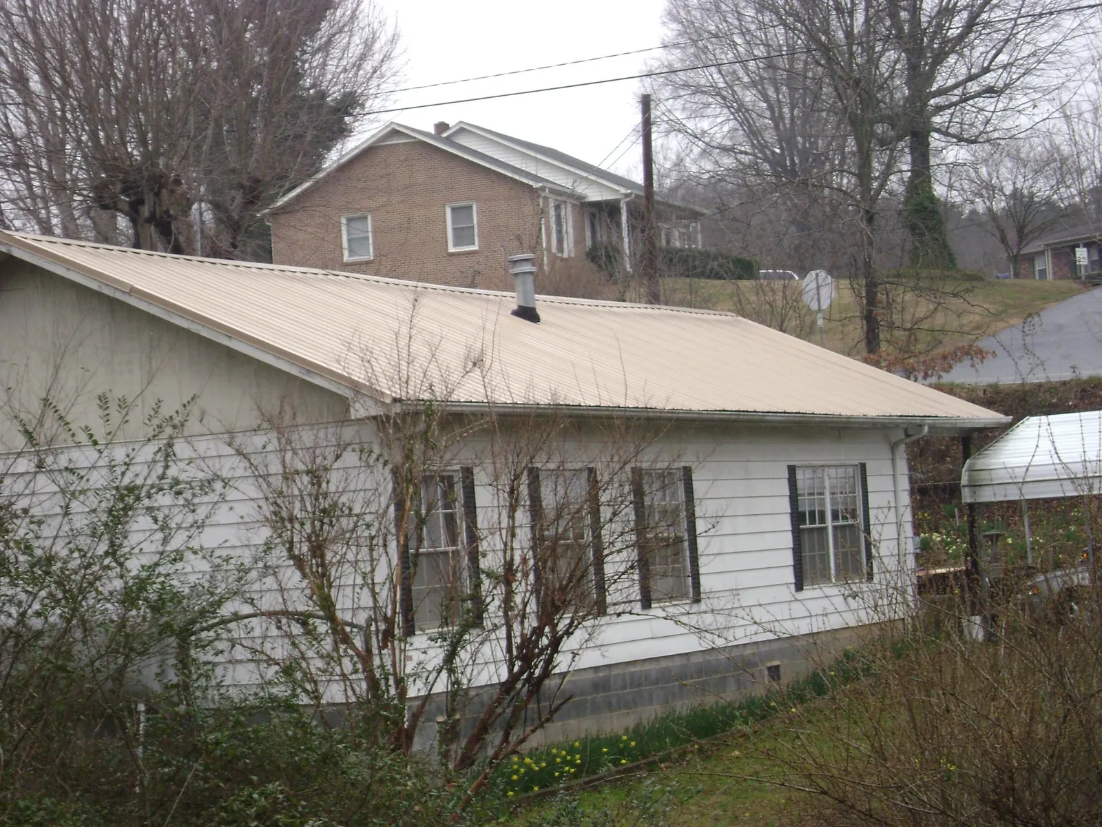Tan metal roof on a white sided house set into a hillside — Commercial Roofing by Roofing Brothers in Morral